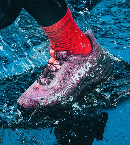 Gros plan d’une personne mettant les jambes dans l’eau en portant des chaussures HOKA.
